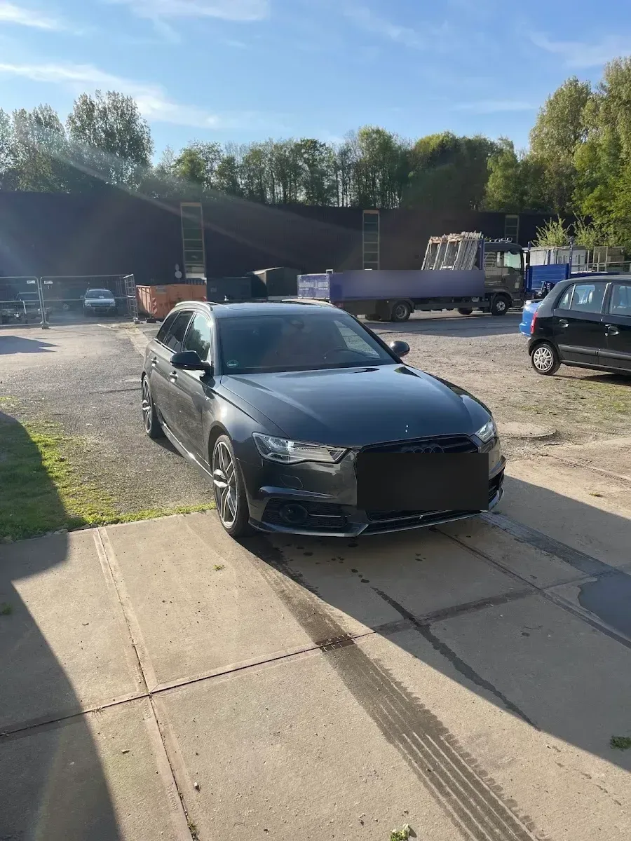 Dunkelgrauer Audi A6 Avant mit S-line-Front und schwarzen Felgen steht im Gegenlicht auf dem Hof des Betriebs, Lack frisch aufbereitet.