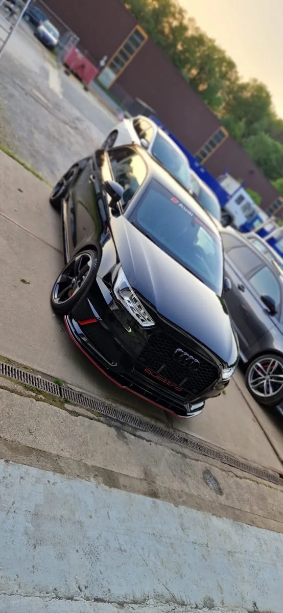 Stark schräg fotografierter schwarzer Audi quattro mit rotem Frontsplitter auf dem Hof neben weiterem Fahrzeug.