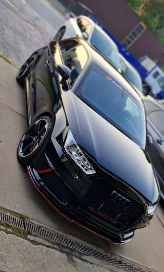 Schwarzer Audi mit Quattro-Wabengrill und roter Frontlippe von schraeg oben, stark spiegelnder Lack, Bild gekippt und mit Vignette bearbeitet.