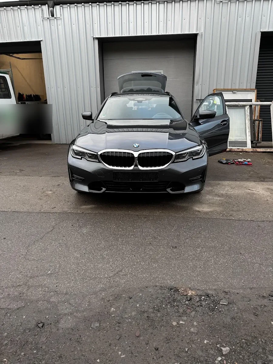 Grauer BMW 3er Touring mit offener Heckklappe und Fahrertuer vor der Aufbereitungshalle, Werkzeug liegt daneben.