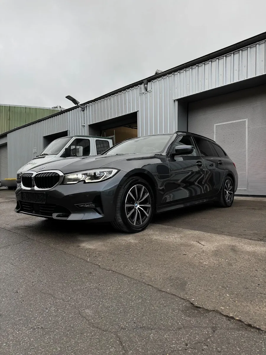 Grauer BMW 3er Touring bei bedecktem Himmel vor der Halle, Lack und Felgen sauber aufbereitet.