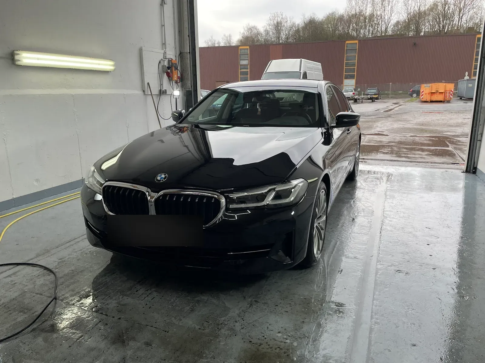 Schwarzer BMW 5er G30 steht frisch handgewaschen und nass glaenzend im Hallentor der Aufbereitungshalle.