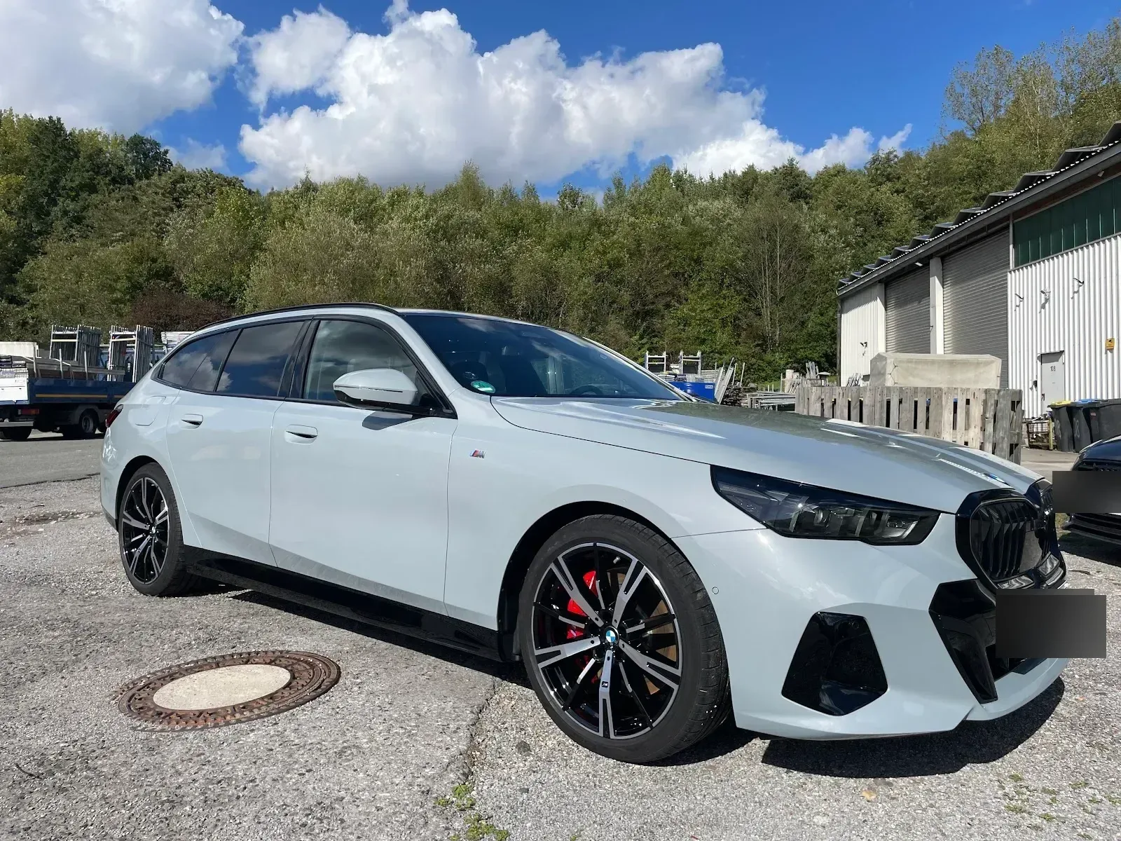 Hellgrauer BMW 5er Touring M-Paket steht komplett aufbereitet und abgabefertig bei Sonnenschein vor der Halle.