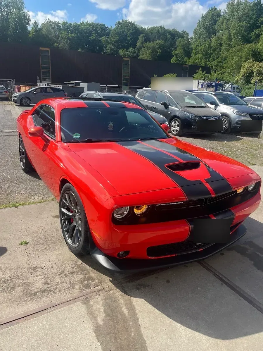 Roter Dodge Challenger mit schwarzen Rallyestreifen im Sonnenlicht auf dem Hof, Lack stark glaenzend nach der Aufbereitung.