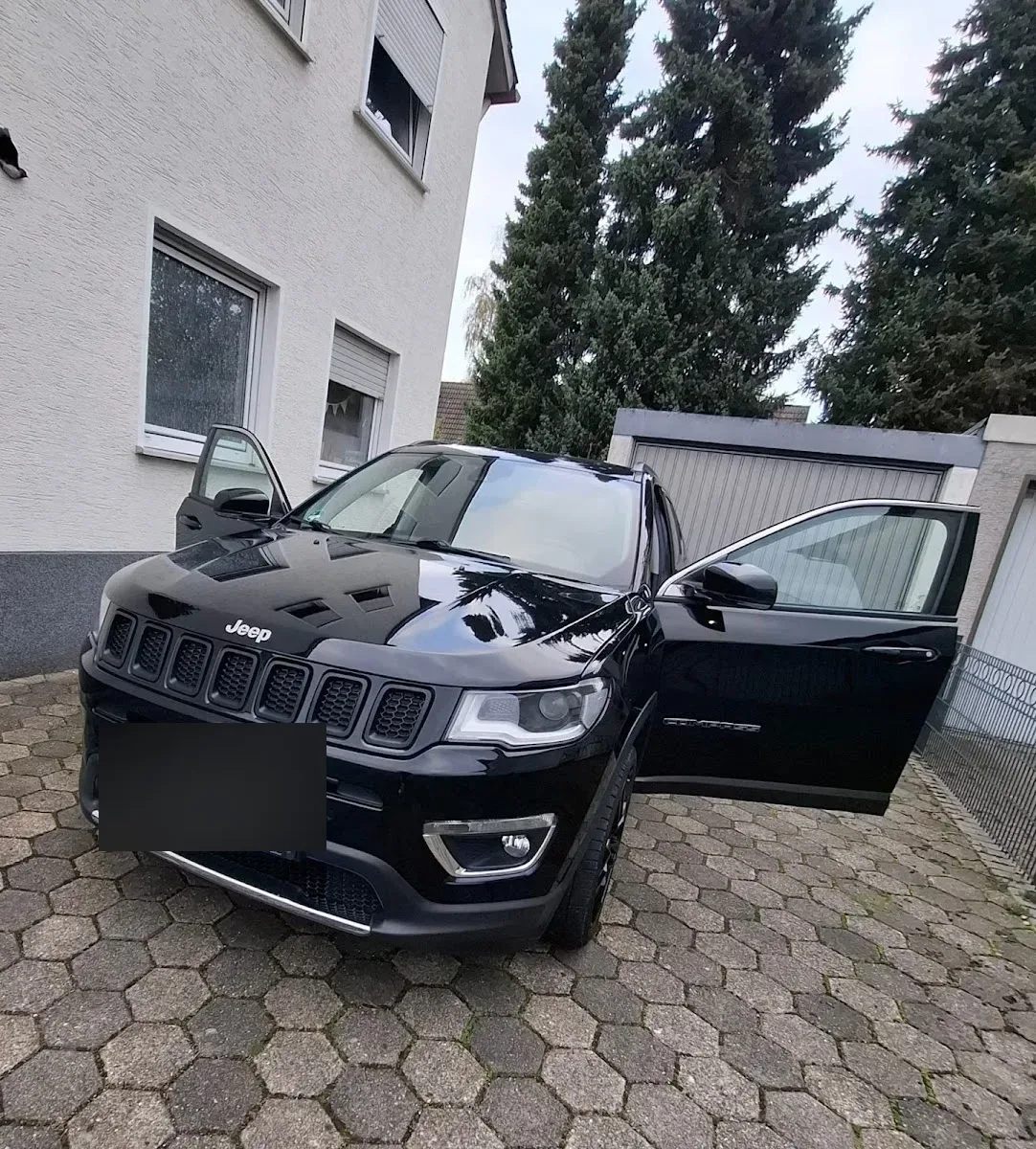 Schwarzer Jeep Compass mit geoeffneten Tueren auf einer gepflasterten Einfahrt, Lack frisch aufbereitet.