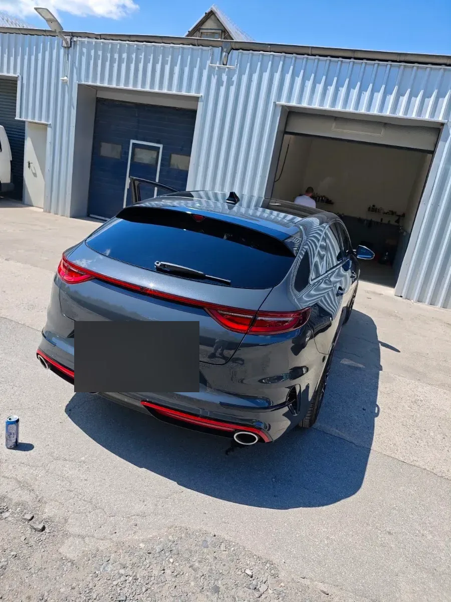 Dunkelgrauer Kia ProCeed GT von hinten vor der Werkstatthalle, Lack spiegelt sauber, Tuer offen.