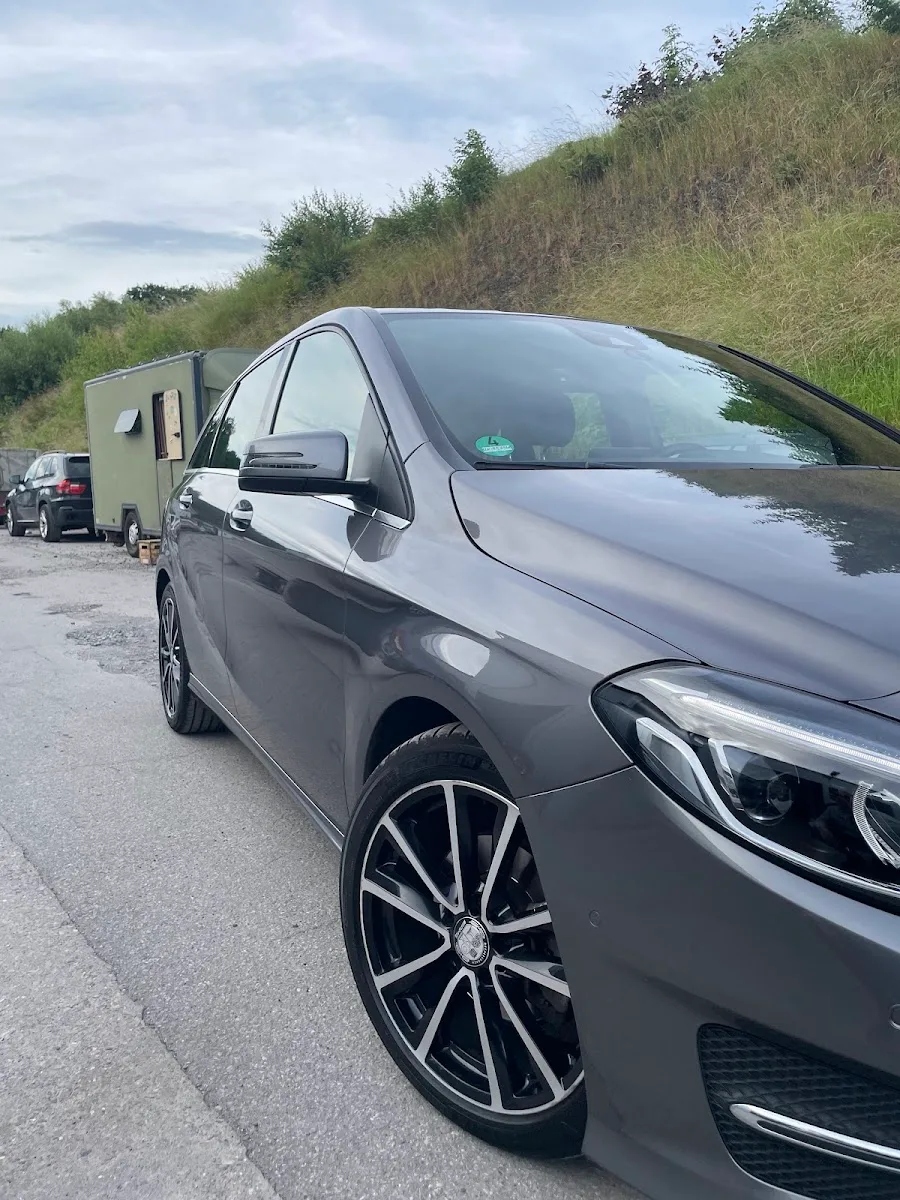 Graue Mercedes B-Klasse von schraeg vorne, Seitenlack spiegelt sauber, bicolor Alufelge im Vordergrund.