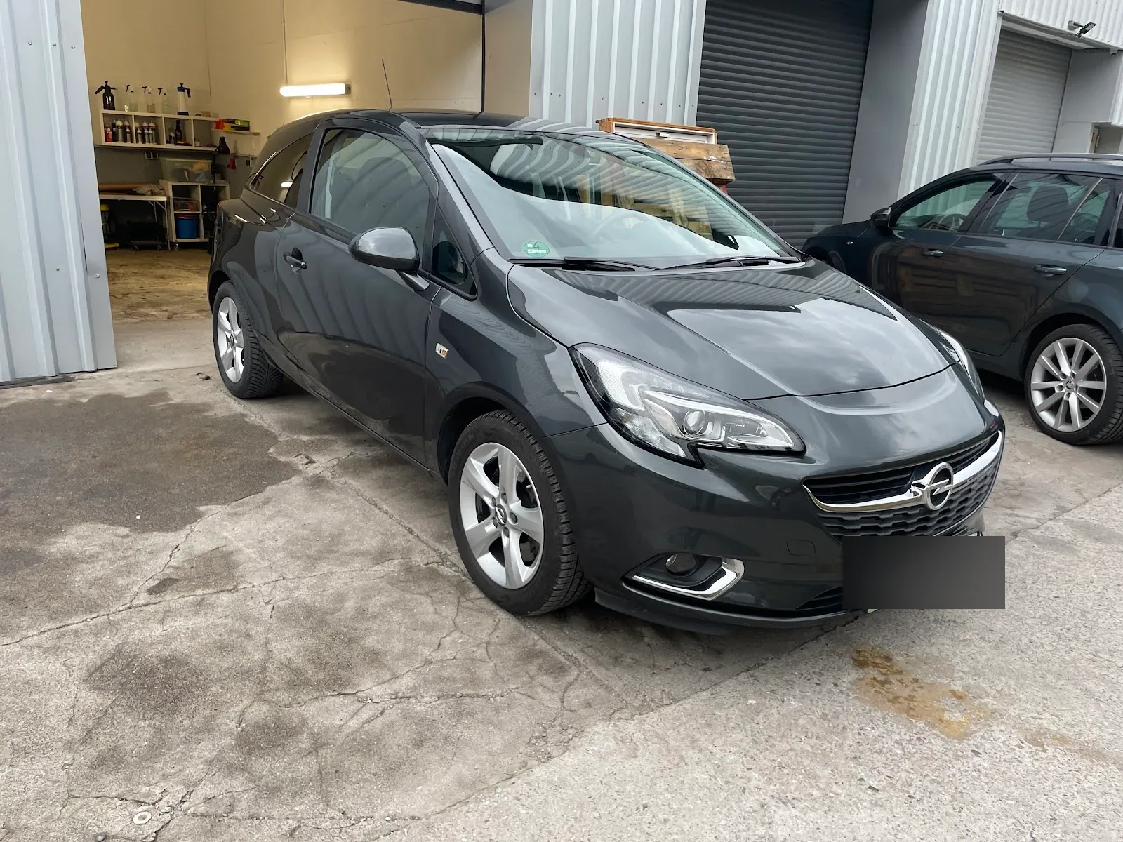 Dunkelgrauer Opel Corsa E in Dreiviertelansicht vor der offenen Hallentuer, Lack frisch aufbereitet.