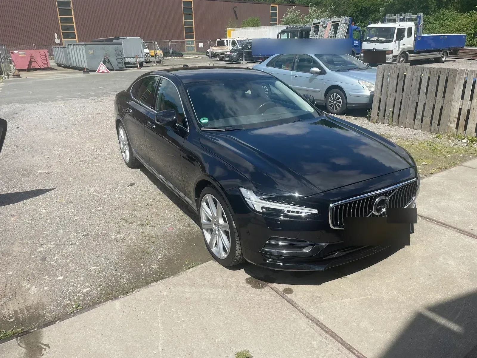 Schwarzer Volvo S90 mit spiegelndem Lack in der Sonne auf dem Hof des Betriebs.