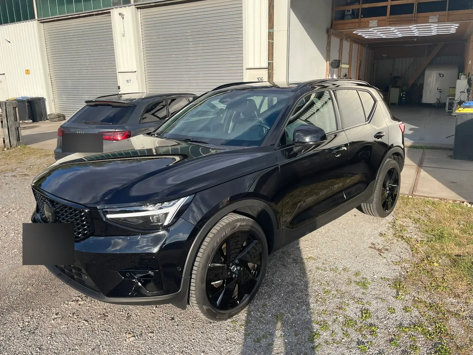 Schwarzer Volvo XC40 in Black-Edition mit spiegelndem Lack steht vor der Aufbereitungshalle mit beleuchteten Hexagon-Lampen im Hintergrund.
