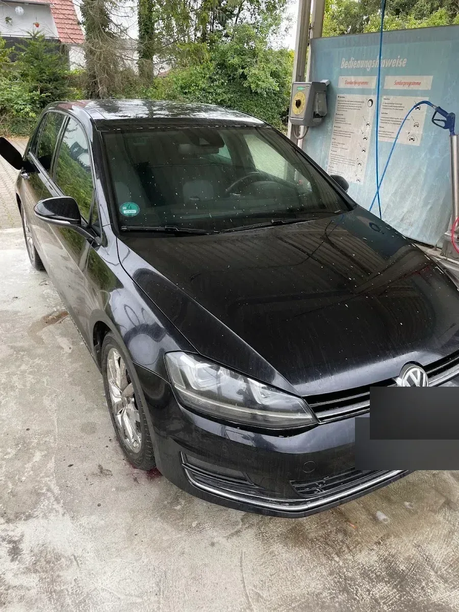 Dunkelgrauer VW Golf 7 an der Waschbox mit deutlich sichtbaren Wasserflecken und Verschmutzung auf Scheibe und Lack.