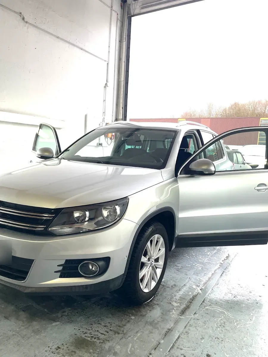 Silberner VW Tiguan mit geoeffneter Beifahrertuer im Waschbereich vor dem offenen Hallentor, Boden noch nass.