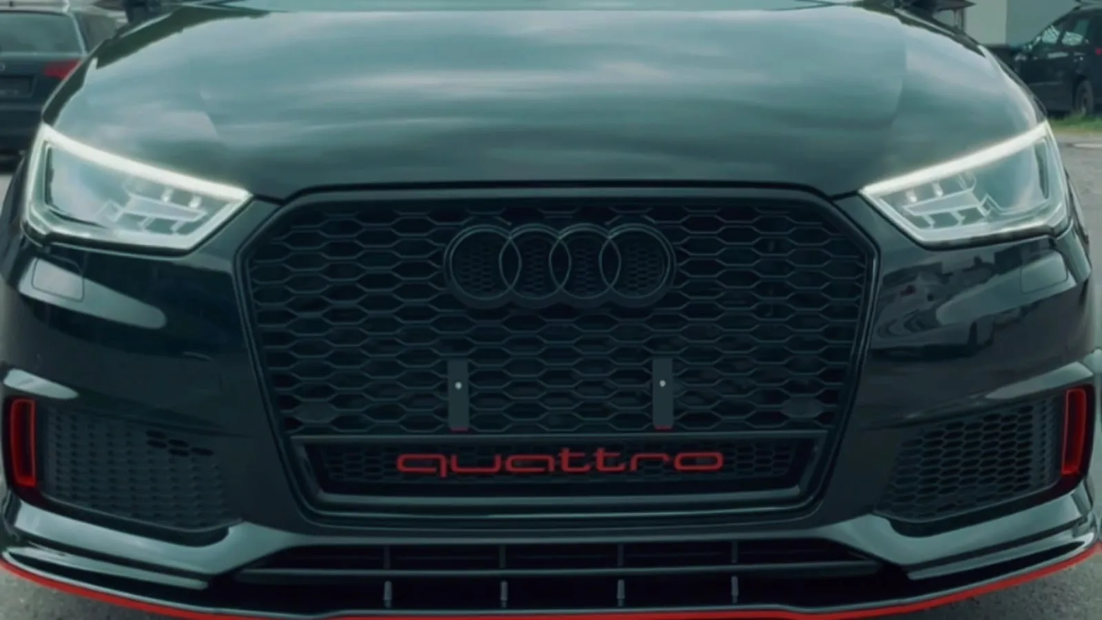 Enge Detailaufnahme von Kuehlergrill, Scheinwerfern und Frontschuerze eines schwarzen Audi RS3 quattro, Lack sauber und glaenzend.