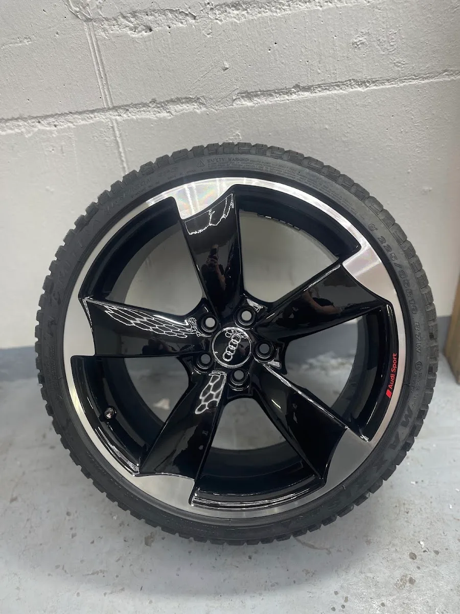 Schwarz glaenzende Audi-Sport-Rotor-Felge mit glanzgedrehtem Rand, an die Wand gelehnt, komplett bremsstaubfrei.