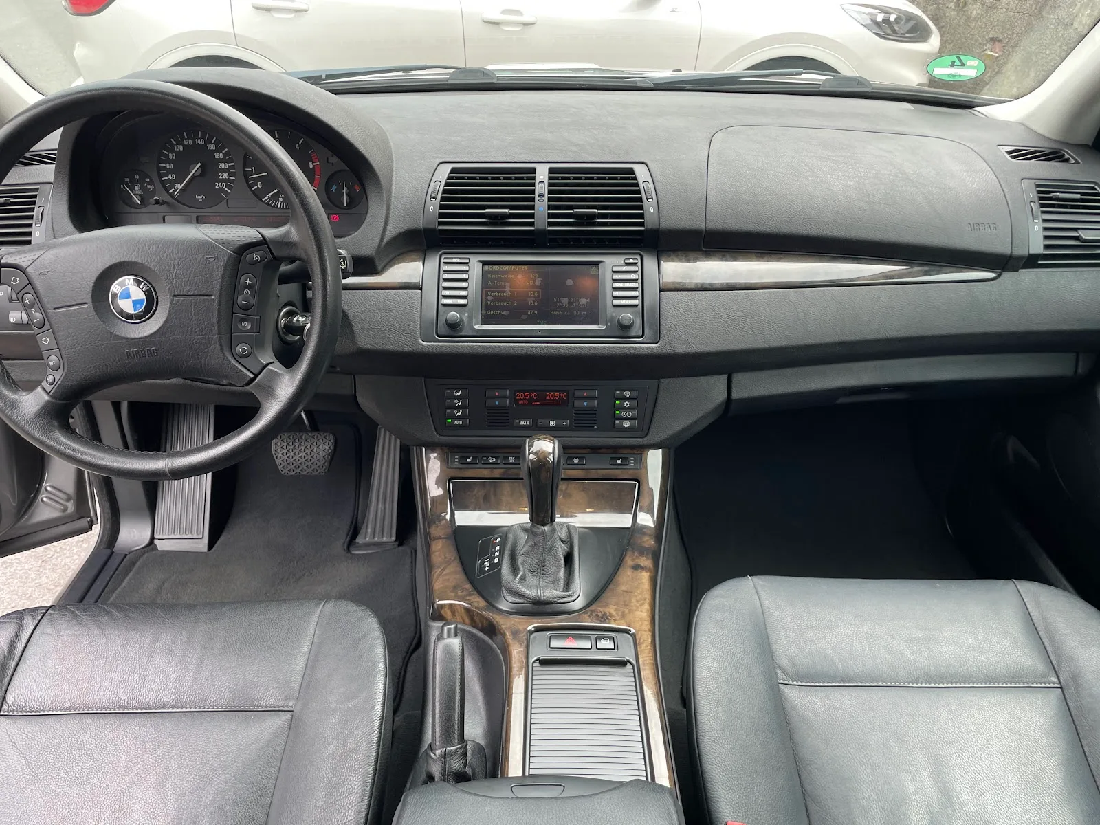 Komplettes Cockpit eines BMW X5 E53 mit schwarzem Leder, Holzdekor und gereinigtem Armaturenbrett, aufgenommen vom Rueckbank-Bereich.
