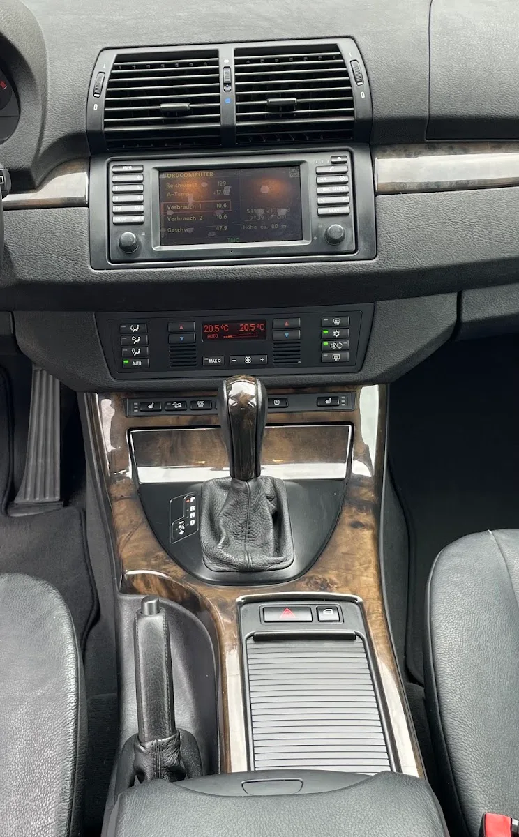 Gereinigte Mittelkonsole und Armaturenbrett eines BMW X5 E53 mit Holzdekor, Bordcomputer-Display und Lederausstattung.