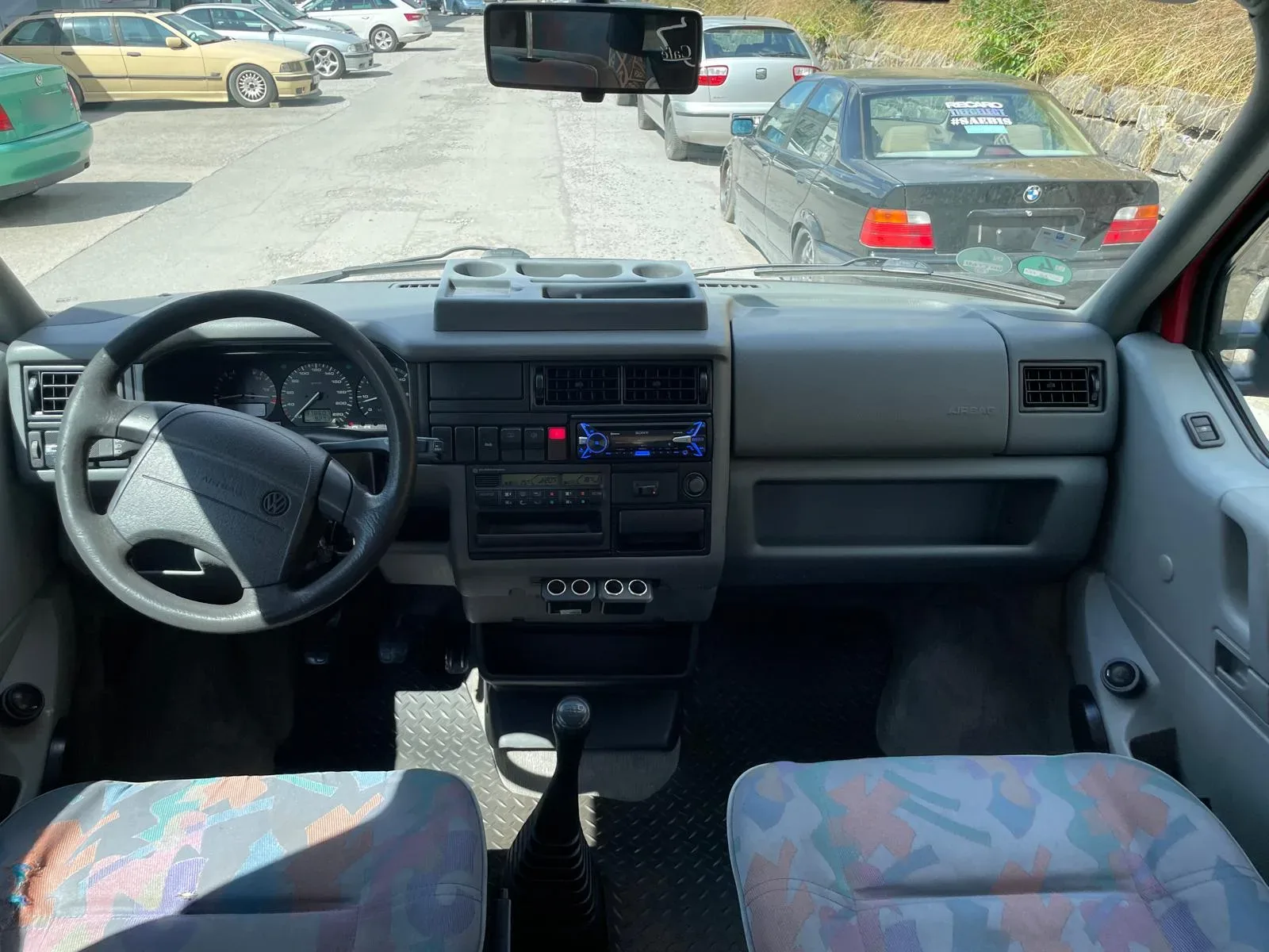 Cockpit eines VW T4 Transporters mit gereinigtem Armaturenbrett, Lenkrad und Stoffsitzen im Mehrfarb-Muster.