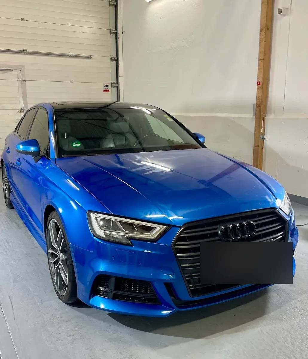 Blauer Audi A3 Limousine S-Line in der Halle, Lack hochglaenzend mit sauberen Spiegelungen auf Haube und Flanke.