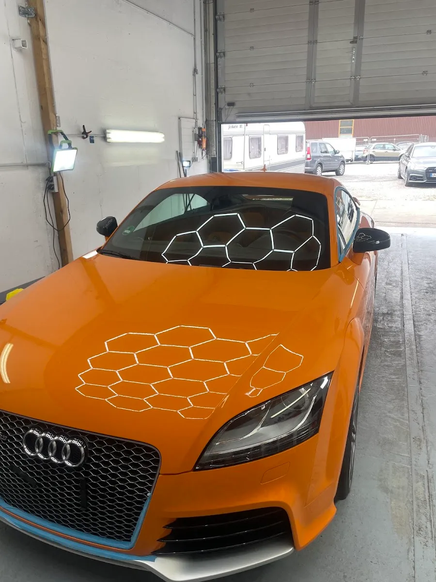 Oranger Audi TT RS in der Halle, auf Haube und Scheibe spiegeln sich die Hexagon-Deckenleuchten im frisch polierten Lack.