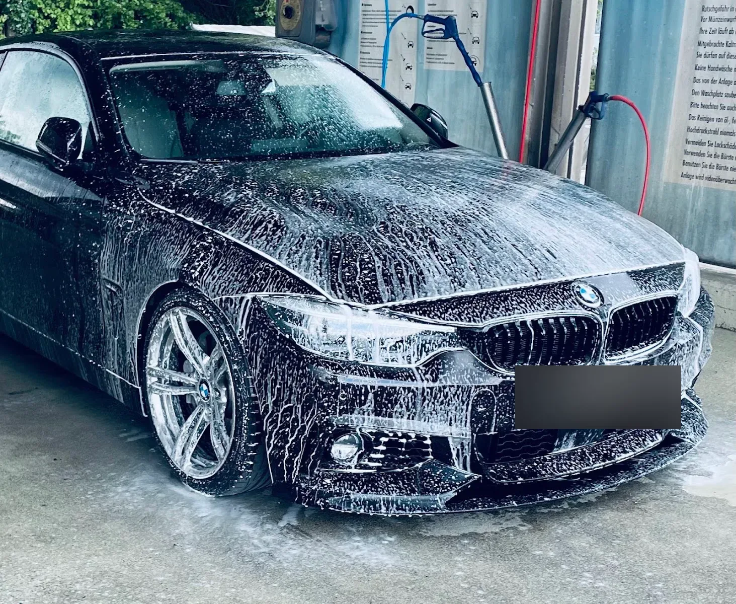 Schwarzer BMW 4er komplett mit Reinigungsschaum eingeschäumt in der Waschbox, Hochdrucklanzen im Hintergrund.