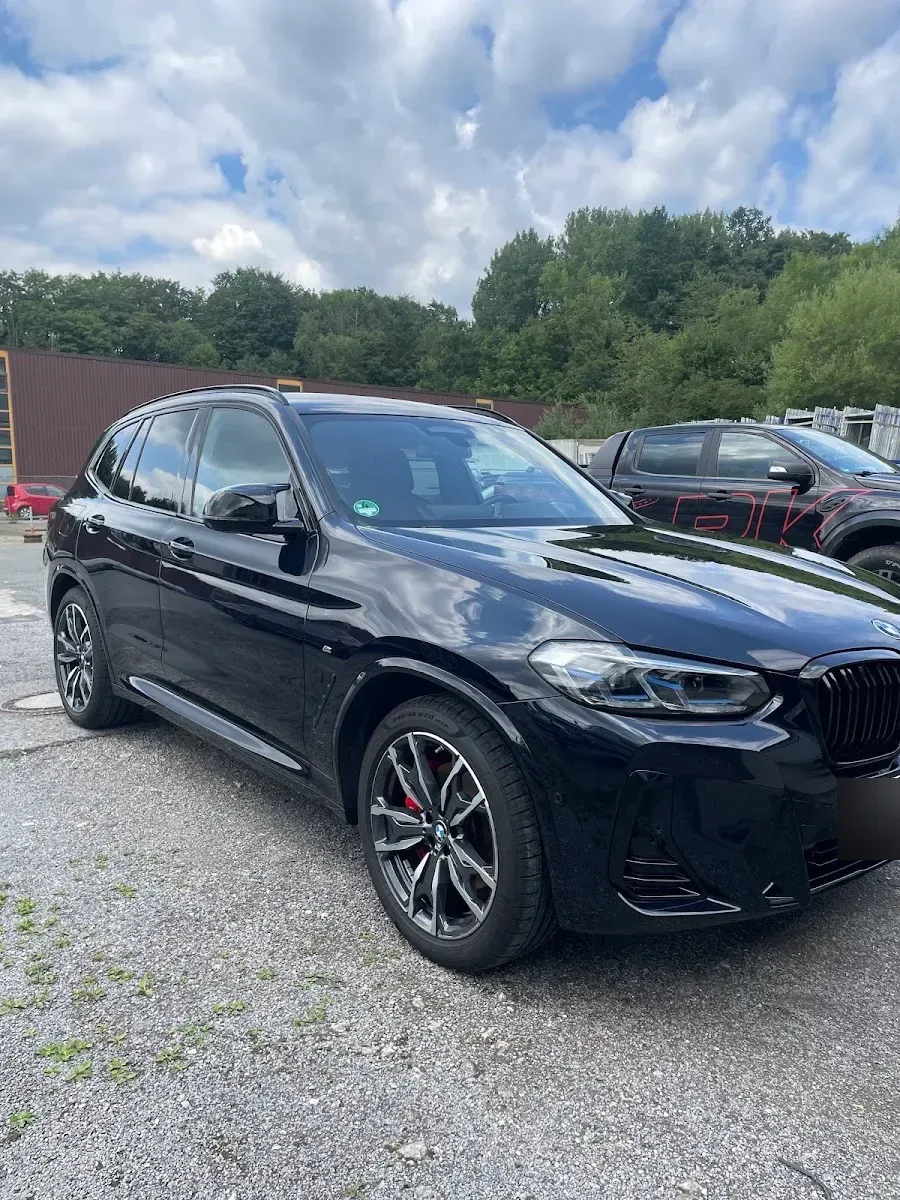 Schwarzer BMW X3 M-Sport im Dreiviertelprofil auf dem Hof, Lack spiegelt Himmel und Wolken klar.