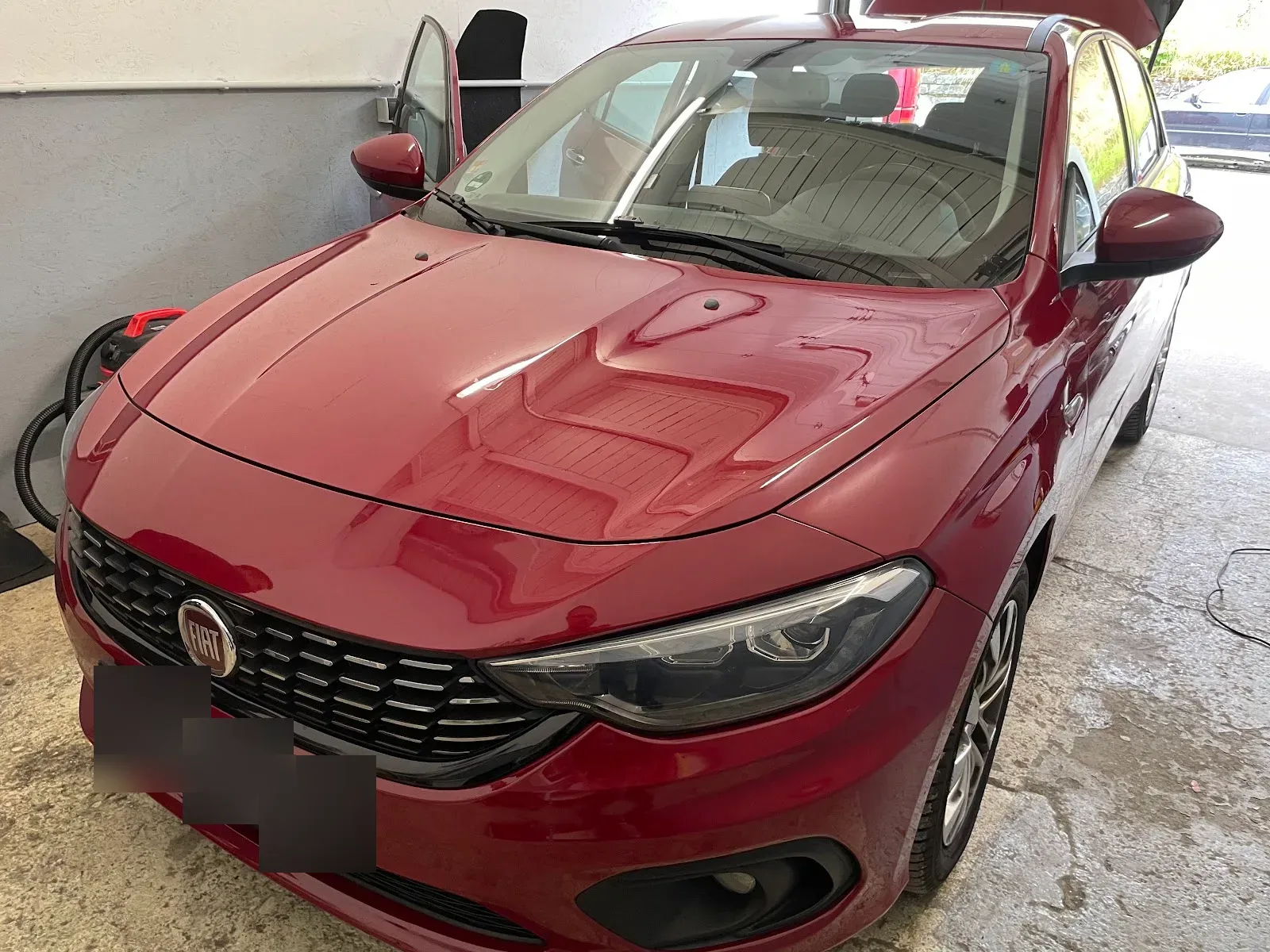 Roter Fiat Tipo Kombi in der Halle mit frisch polierter, stark spiegelnder Motorhaube, Sauger-Schlauch daneben.
