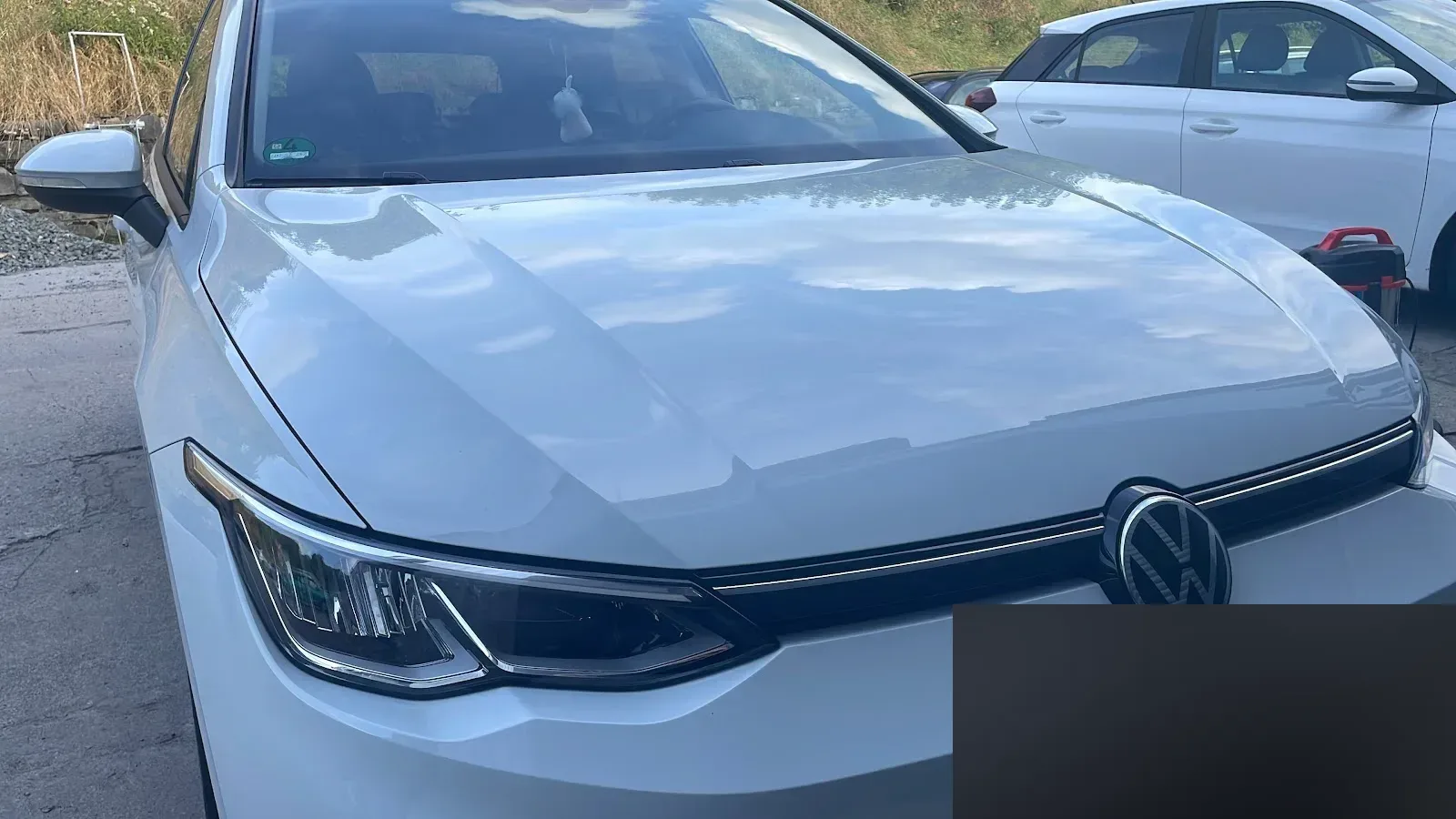 Nahaufnahme der Motorhaube und Front eines weissen VW Golf 8, in der der Himmel sich klar spiegelt.