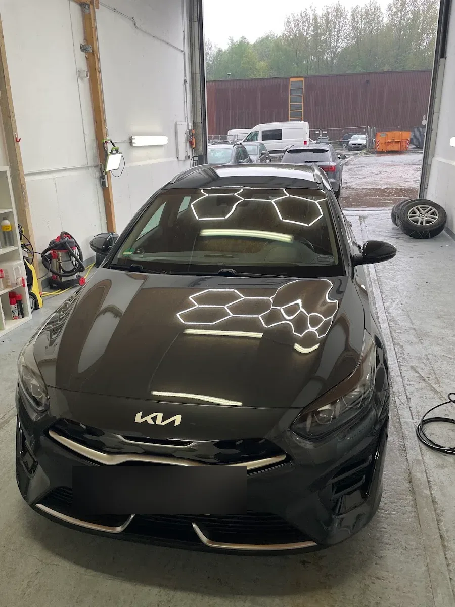 Dunkelbrauner Kia Ceed frontal in der Halle, Haube und Dach spiegeln das Waben-LED-Muster nach der Politur.