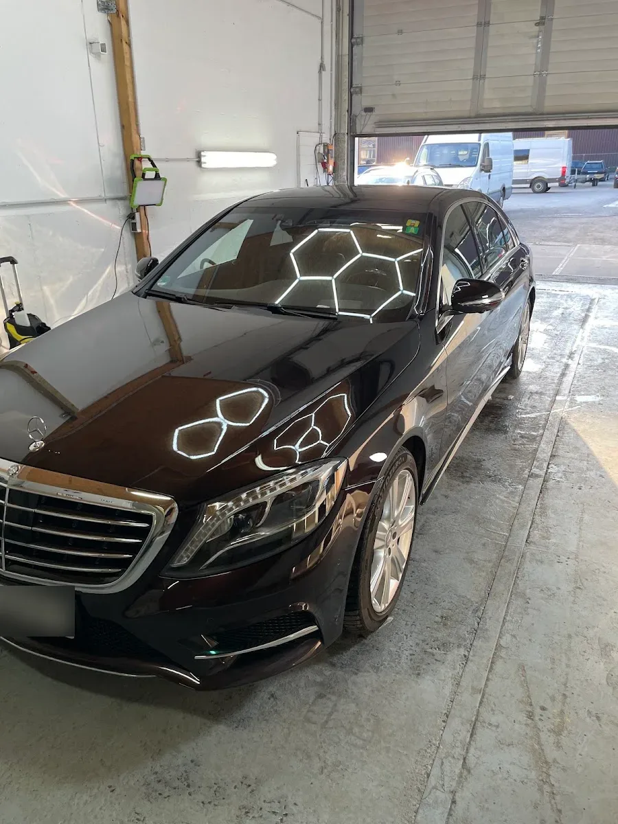 Dunkelbraun-metallic Mercedes S-Klasse in der Halle, Hexagon-Licht spiegelt sich klar in Motorhaube und Flanke.