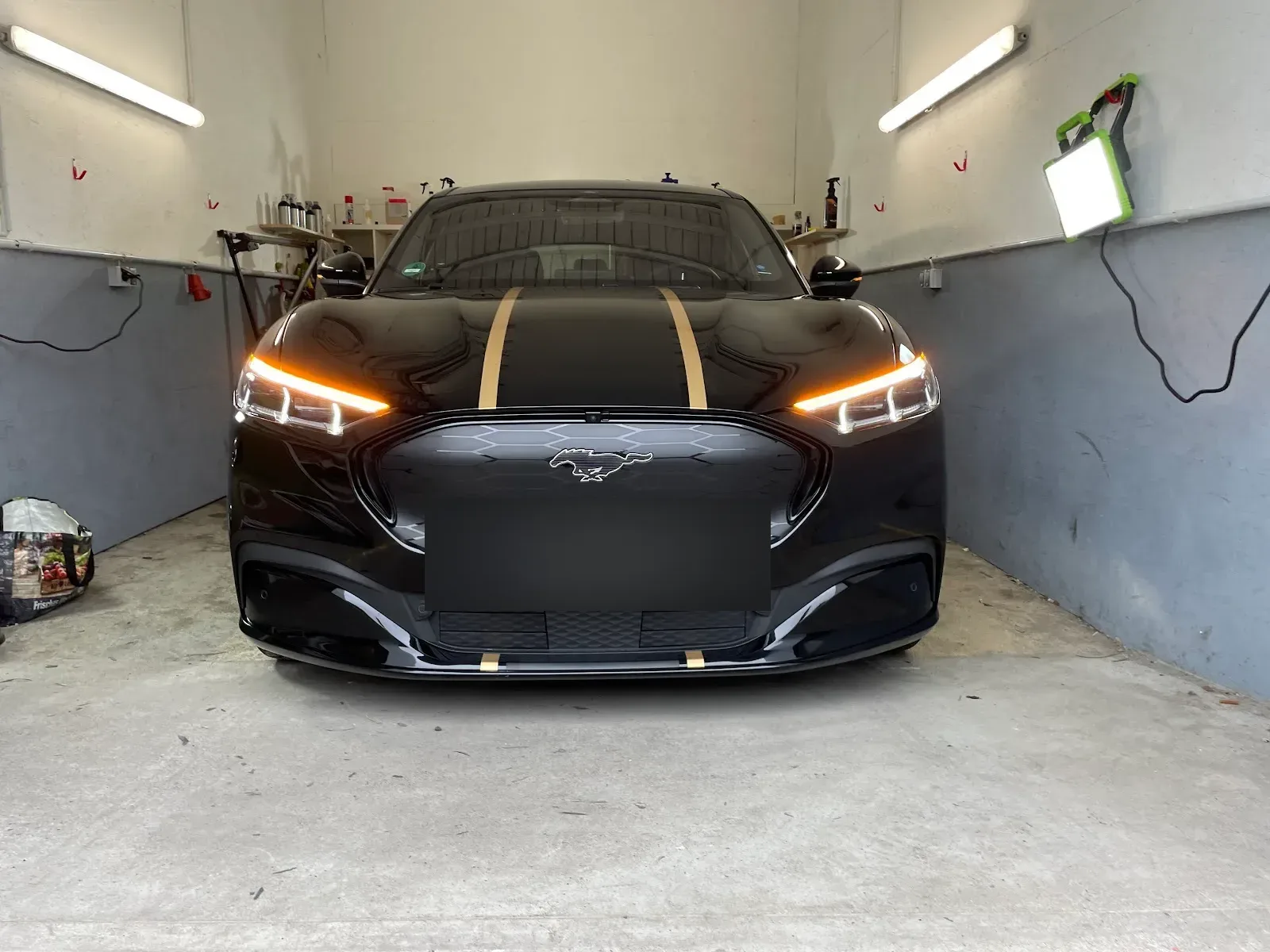 Schwarzer Ford Mustang Mach-E frontal in der Halle, Haube und Frontspoiler mit Klebeband abgeklebt als Vorbereitung fuer Politur bzw. Versiegelung.
