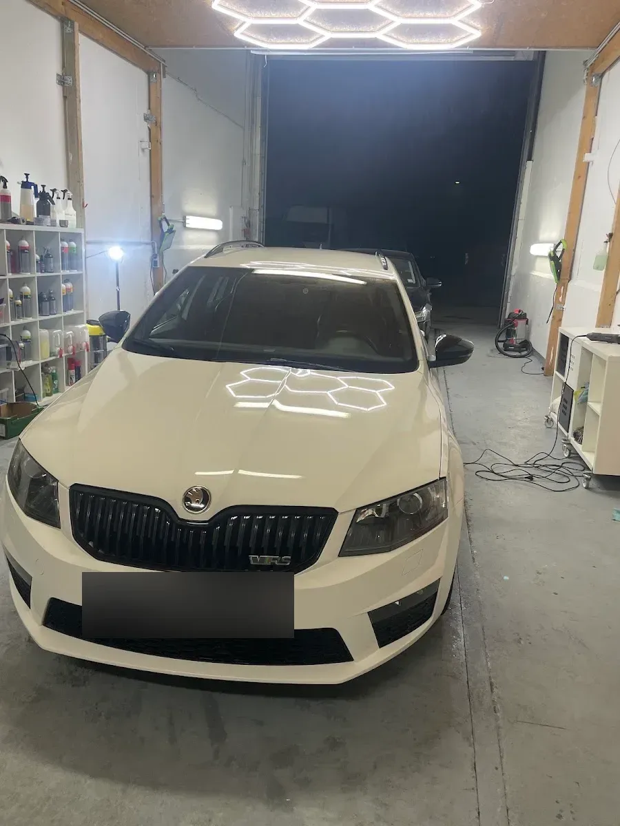 Weisser Skoda Octavia RS Kombi in der Halle unter der Waben-LED-Beleuchtung, Haube spiegelt das Lichtmuster.