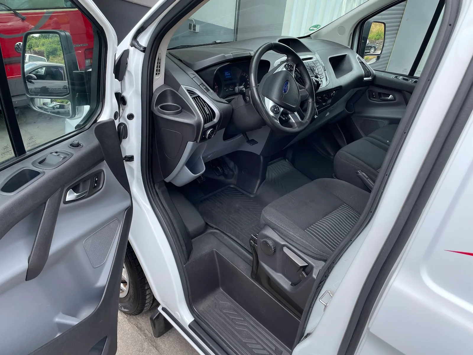 Offene Fahrertür eines weissen Ford Transit Custom mit sauberem Cockpit, gereinigten Stoffsitzen und ausgesaugtem Fussraum.