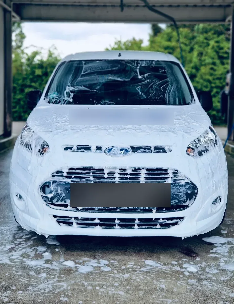 Weisser Ford Transit Connect Firmenwagen komplett mit Waschschaum eingeschaeumt in der Waschbox, Frontansicht.