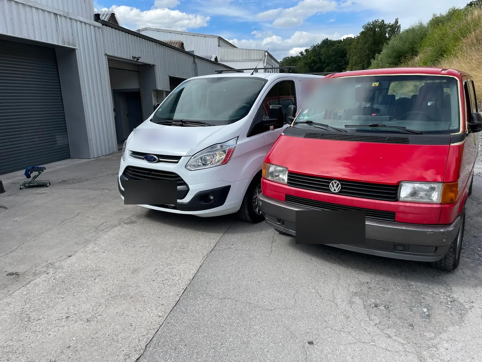 Weisser Ford Transit Custom mit Firmenbeschriftung und roter VW T4 Bus stehen nebeneinander vor der Halle.
