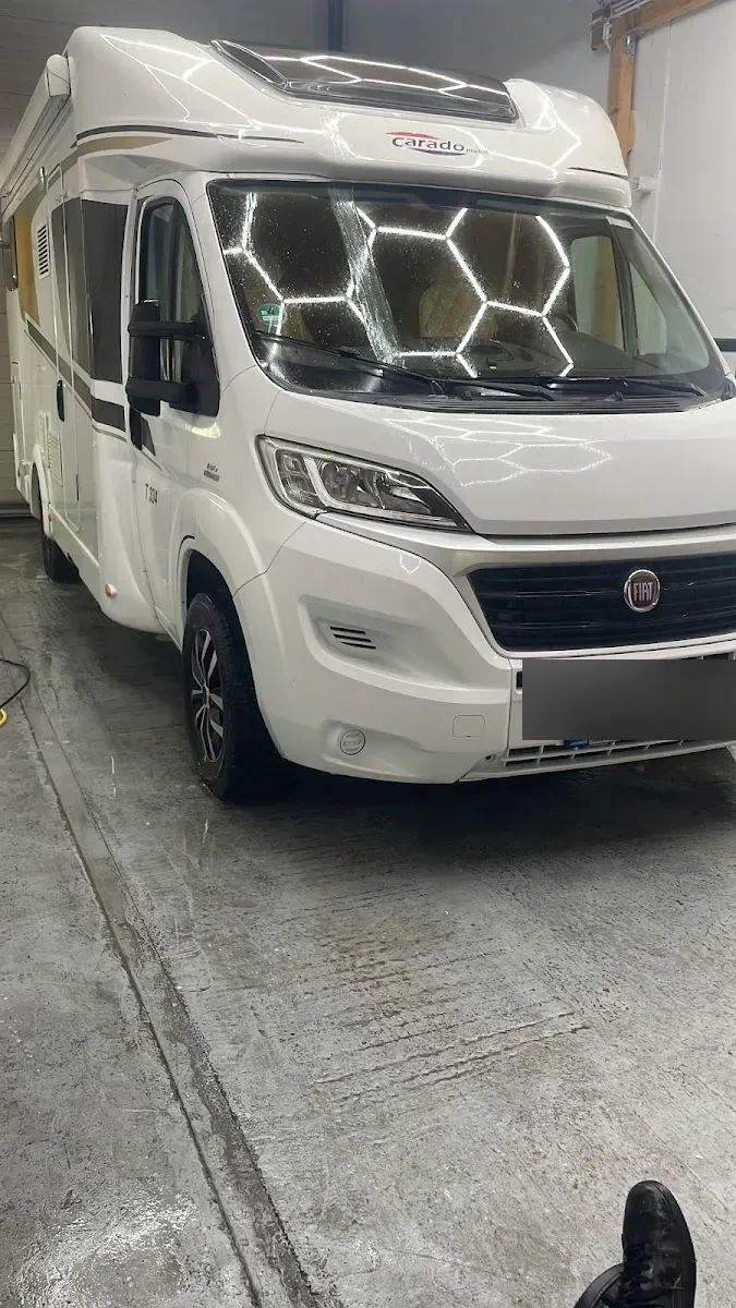 Weißes Carado-Wohnmobil auf Fiat-Ducato-Basis frontal in der Halle unter Hexagon-Licht, frisch gewaschen mit nassem Boden.
